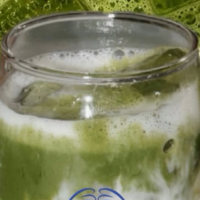 Fragola matcha en vaso de vidrio: matcha latte verde intenso con espuma sobre compota de fresa