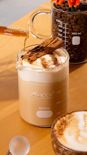 Latte con canela en vaso de precipitado de 500 ml mientras le vierten jarabe desde un tubo de ensayo
