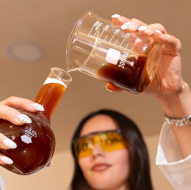 Barista con lentes de laboratorio vertiendo café de un vaso a un matraz