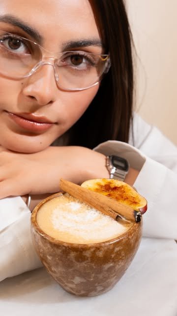 Latte con arte en taza de cerámica, rodaja de manzana caramelizada y raja de canela