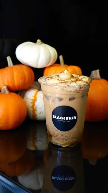 Pumpkin Latte helado con foam de calabaza y canela en vaso Black Rush, rodeado de calabazas sobre fondo negro