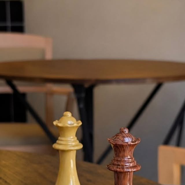 Dos reinas de ajedrez, una clara y una de madera, sobre una mesa de Bosco Café