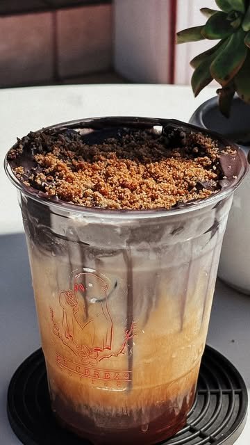 Vaso del Cerezo Muerto: latte de coldbrew con capa oscura de ceniza y crumble dorado encima, el logo del Cerezo impreso en el vaso