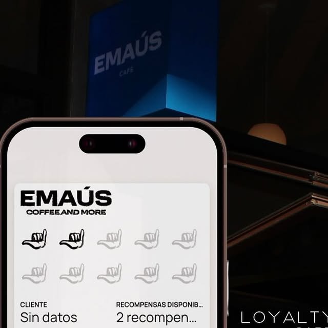 Celular con la tarjeta digital de sellos shaka frente al letrero azul de EMAÚS