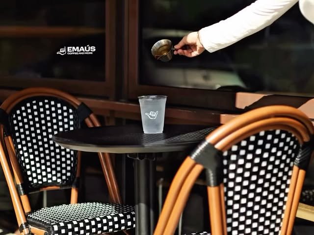 Vaso de americano frío sobre mesa negra entre sillas bistró tejidas