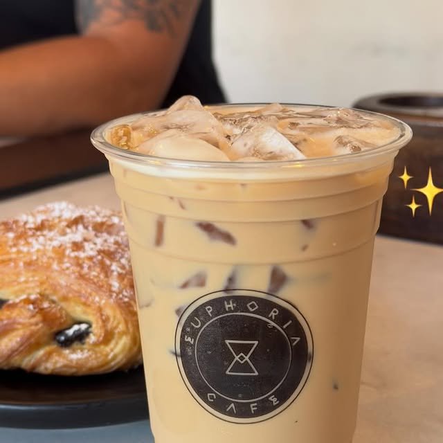 Latte con hielo en vaso con el logo de Euphoria junto a un pan hojaldrado de chocolate espolvoreado con azúcar