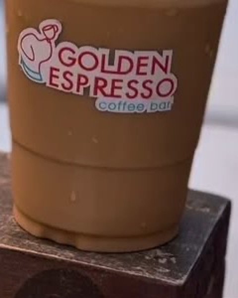 Vaso de café helado con el logo de Golden Espresso sobre el descansabrazos de madera de la terraza