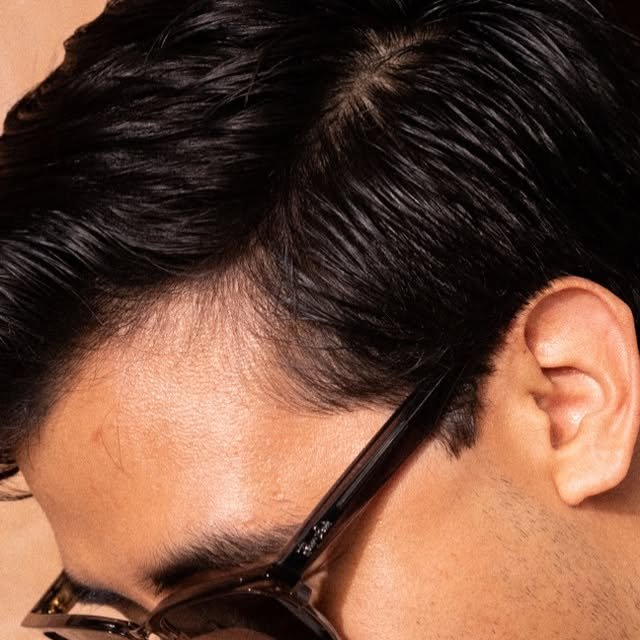 Acercamiento al cabello peinado y los lentes de un integrante del equipo