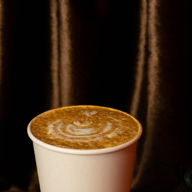Pumpkin Spice Latte caliente con latte art y canela, frente a una cortina de terciopelo café