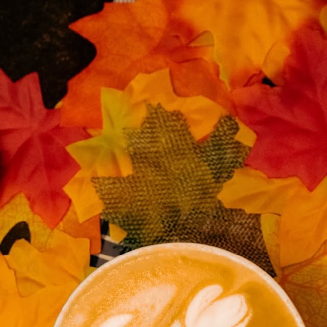 Pumpkin Spice Latte con latte art sobre hojas de otoño