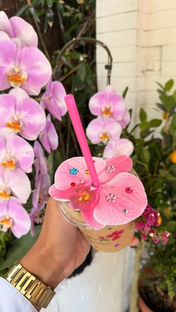 Bebida helada de El Rincón de Leo coronada con una orquídea rosa con brillos, frente a un muro de orquídeas