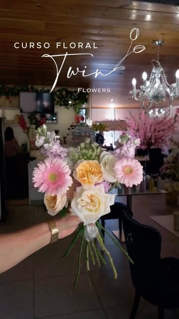 Ramo de gerberas rosas, rosas durazno y blancas sostenido en el salón del curso floral, con candelabro de cristal al fondo