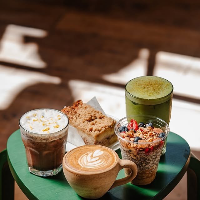 Favoritos de temporada de Unity sobre la mesa verde: latte con arte, matcha, mocha con espuma, parfait con frutos rojos y una barra de crumble